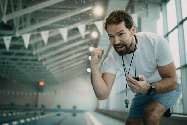 Mid- adult man instructor with stopwatch encouraging swimmer during training.