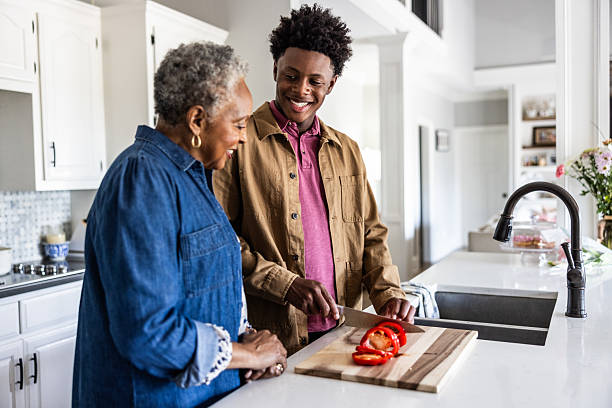 Senior woman helping teenage grandson cut vegetables in kitchen