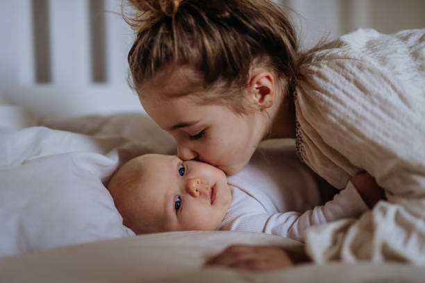 Sisterhood. Portrait of big sister holding, carefully cuddling, kissing baby sister. Sisterly love, joy for new family member.